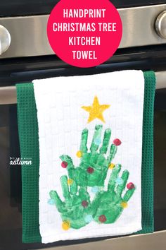 a handprint christmas tree towel hanging on the oven door with text overlay that reads, handprint christmas tree towel