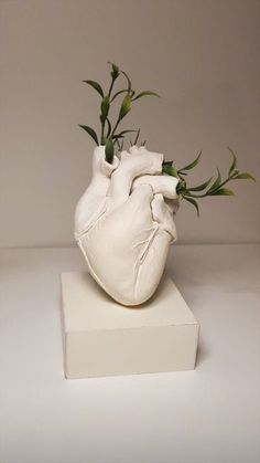 a white heart shaped vase with green stems sticking out of it's back end