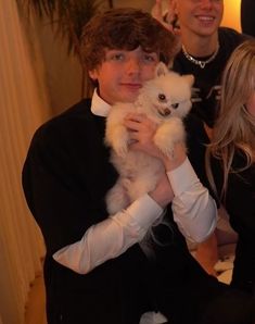 two people are holding a small white dog