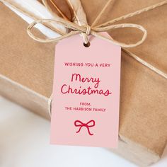 a pink christmas gift tag sitting on top of a brown box with a red ribbon