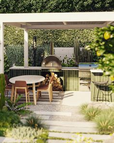 an outdoor kitchen and dining area with wood stacked on the table, surrounded by greenery