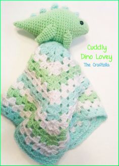 a crocheted green and white stuffed animal laying on top of a blanket with the words cuddly dino lovey written above it