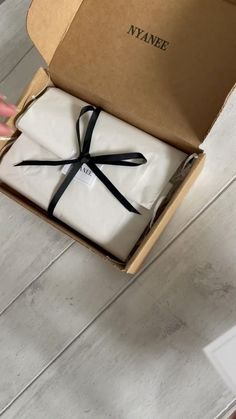 an open box with two folded white sheets and a black ribbon tied around the edges