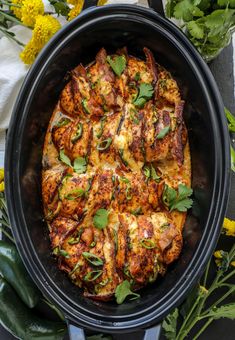 a pan filled with chicken covered in sauce and garnished with fresh herbs, surrounded by yellow flowers