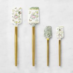 three gold colored toothbrushes with floral designs on them, one is white and the other is green