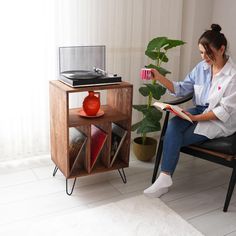 a woman sitting in a chair reading a book next to a potted plant and record player