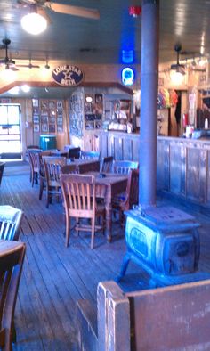 the inside of a restaurant with wooden tables, chairs and an old fashioned wood stove