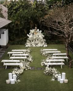 an outdoor ceremony set up with white flowers and candles on the grass in front of trees