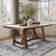 a wooden table sitting on top of a rug in front of two windows with large windows