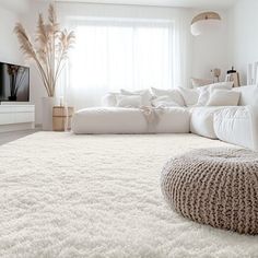 a living room with a large white rug on the floor next to a couch and television