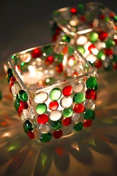 two glass candle holders with christmas decorations on them and lights shining in the back ground