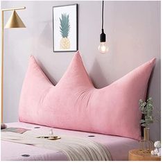 a pink pillow sitting on top of a bed next to a lamp and a painting