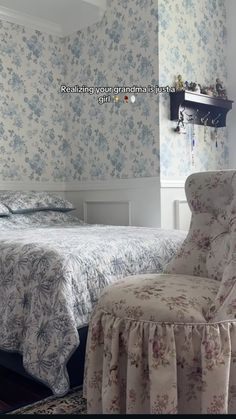 a bed sitting next to a chair in a room with floral wall paper on the walls