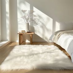 a white bed sitting in a bedroom next to a wooden table with a vase on top of it