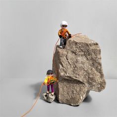 two figurines sitting on top of a rock next to each other, one holding a rope