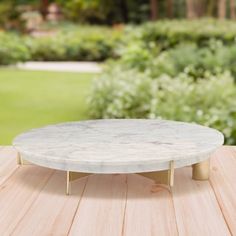 a white marble coffee table sitting on top of a wooden deck in front of some bushes