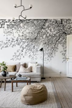 a living room with white furniture and a large tree mural on the wall behind it