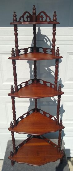 three tiered wooden shelf sitting in front of a garage door with a shadow on the wall