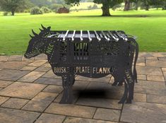 a metal cow sculpture sitting on top of a brick floor next to a tree and grass covered field