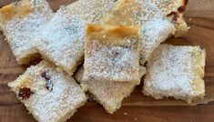 several pieces of dessert sitting on top of a wooden cutting board with powdered sugar