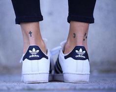 a person with tattoos on their feet wearing white and black adidas sneakers