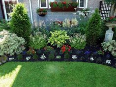 a garden with lots of flowers and plants in the front yard, next to a house