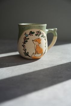 a ceramic cup with a fox painted on the side sitting on top of a table