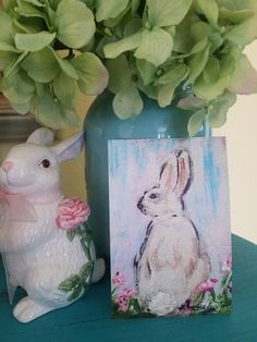 a painting of a rabbit next to a vase with flowers in it on a table