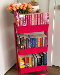 there is a pink book shelf with books on it and flowers in the vase next to it