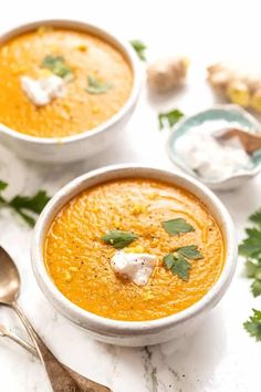 two bowls of carrot soup with sour cream and parsley garnish on top