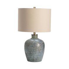 a table lamp with a white shade on the base and a light blue vase underneath it