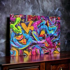 a colorful painting on top of a wooden table next to a wall with graffiti written on it