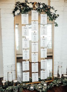 a table with candles and place cards on it, along with greenery in front of a mirror