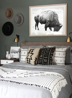 a bed with pillows and blankets on top of it in front of a framed buffalo print