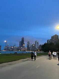 people are walking on the sidewalk in front of a cityscape at night time