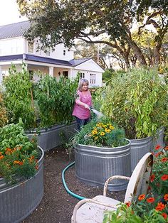 a woman is watering her garden in the middle of an outdoor area with lots of potted plants