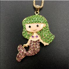 a necklace with a little mermaid holding a fish on it's back and green hair