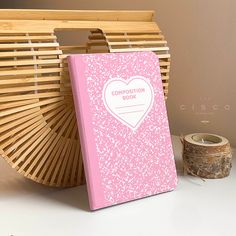 a pink book sitting on top of a table next to a basket and candle holder