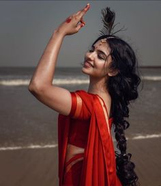 a woman in an orange sari is standing on the beach and pointing to something