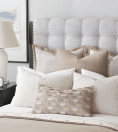 a bed with white and beige pillows on it's headboard, next to a night stand