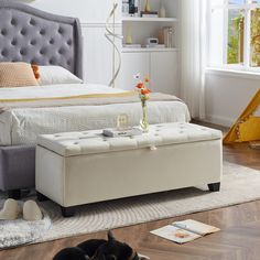 a dog laying on the floor in front of a bed with a tufted headboard and footstool