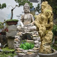 a buddha statue sitting on top of a stone wall next to a potted plant