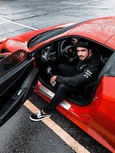 a man sitting in the driver's seat of a red sports car