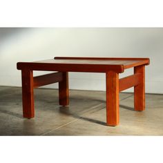 a small wooden table sitting on top of a cement floor next to a white wall