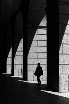 black and white photograph of man walking under arches