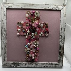 a cross made out of beads and other items in a frame on a table next to a wall