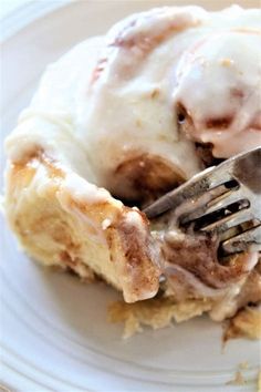 a piece of cinnamon roll on a white plate with a fork in it and icing