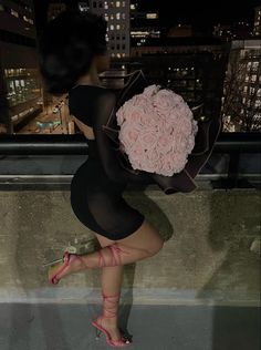 a woman holding a bouquet of flowers on top of a building in the city at night