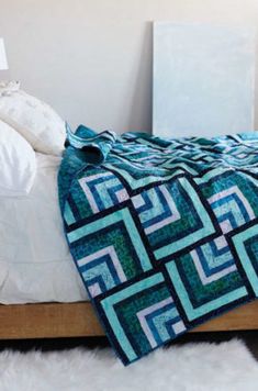 a bed topped with a blue and green quilt on top of a wooden headboard