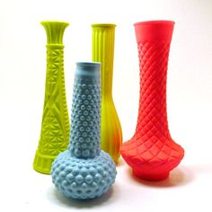 four different colored vases sitting next to each other on a white surface with no one around them